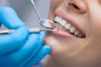 The image shows a person receiving dental care, with a dental hygienist using a dental instrument to clean teeth while the patient is smiling.