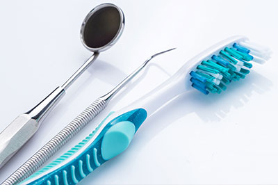 The image shows a collection of dental tools, including a toothbrush and various other instruments, placed on a white surface.