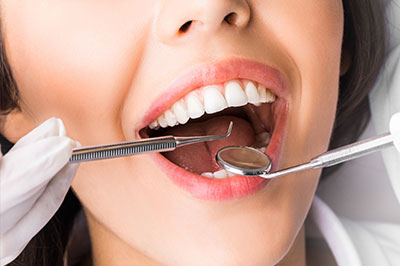 A woman wearing a white lab coat and holding dental instruments to her mouth, with a focus on the teeth cleaning process.