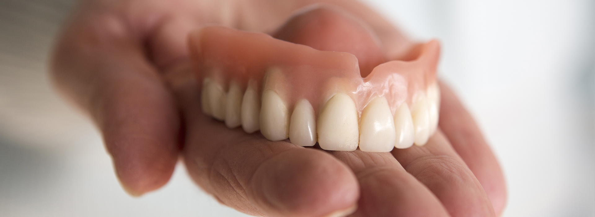 The image shows a person holding up a set of dentures, displaying the upper and lower teeth.