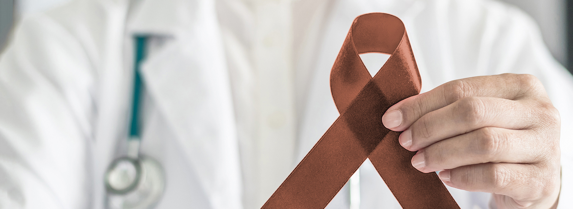 The image shows a person in a medical uniform holding up a red ribbon with a white stripe, symbolizing awareness for a health condition.