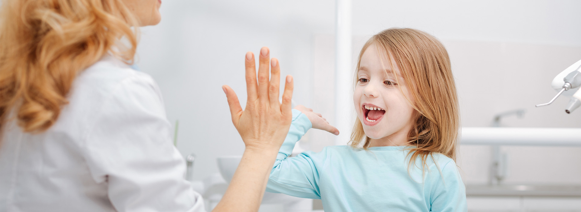 A woman and a young girl in a dental office, with the woman gesturing towards the child.
