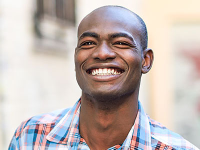 A smiling man with a shaved head, wearing a blue and white plaid shirt.
