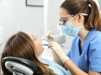 A dental hygienist in a professional setting, performing a teeth cleaning procedure on a patient.