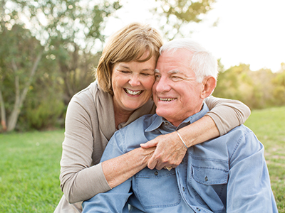 An elderly couple sharing a warm embrace outdoors during daylight.