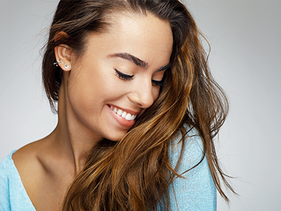 Smiling woman with long hair, wearing a blue top, against a light background.