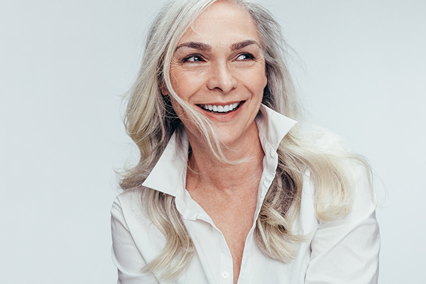 The image shows a woman with short hair, wearing a white top, smiling at the camera.