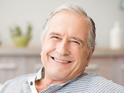 A smiling older man with gray hair, wearing a blue shirt and sitting in a relaxed pose.