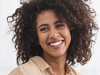 A woman with curly hair smiling, against a white background.