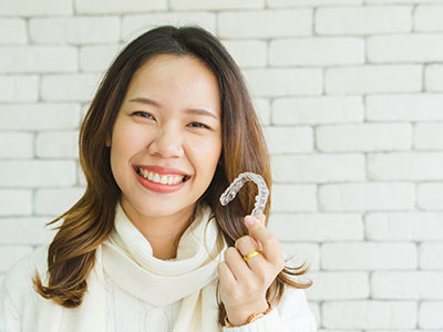 A smiling woman holding a dental implant in her hand.